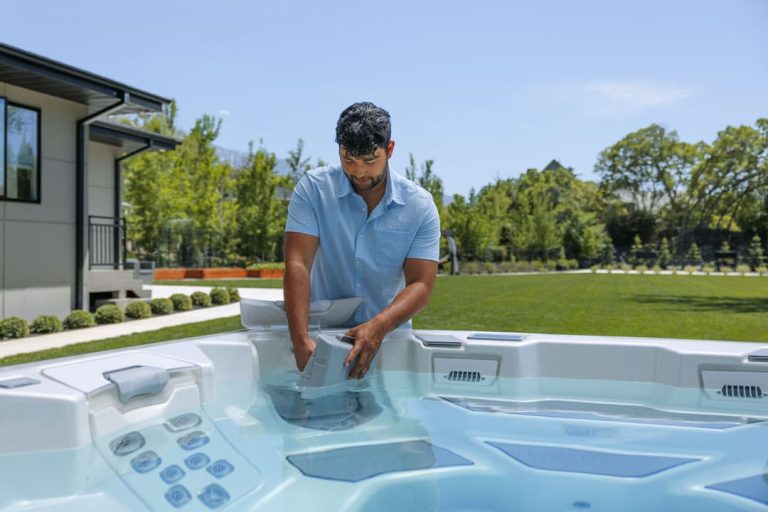 A man is shown replacing a hot tub filter. He is wearing a light blue collared shirt and is standing in a backyard next to the hot tub that he is providing maintenance on.