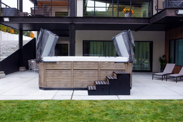 A swim spa outdoors in a backyard has the lid halfway open.